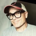 Joseph "JK" Kalinowski is wearing a baseball hat, black glasses, and a grey t-shirt.